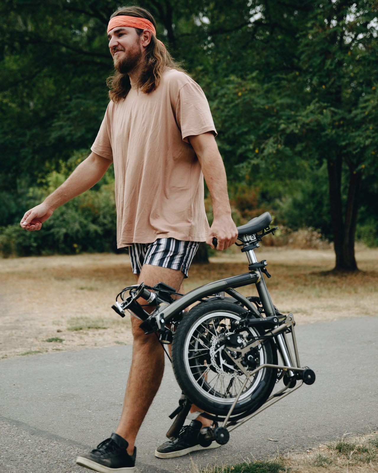 ชายเดินถือจักรยานพับ Brompton ในสวน